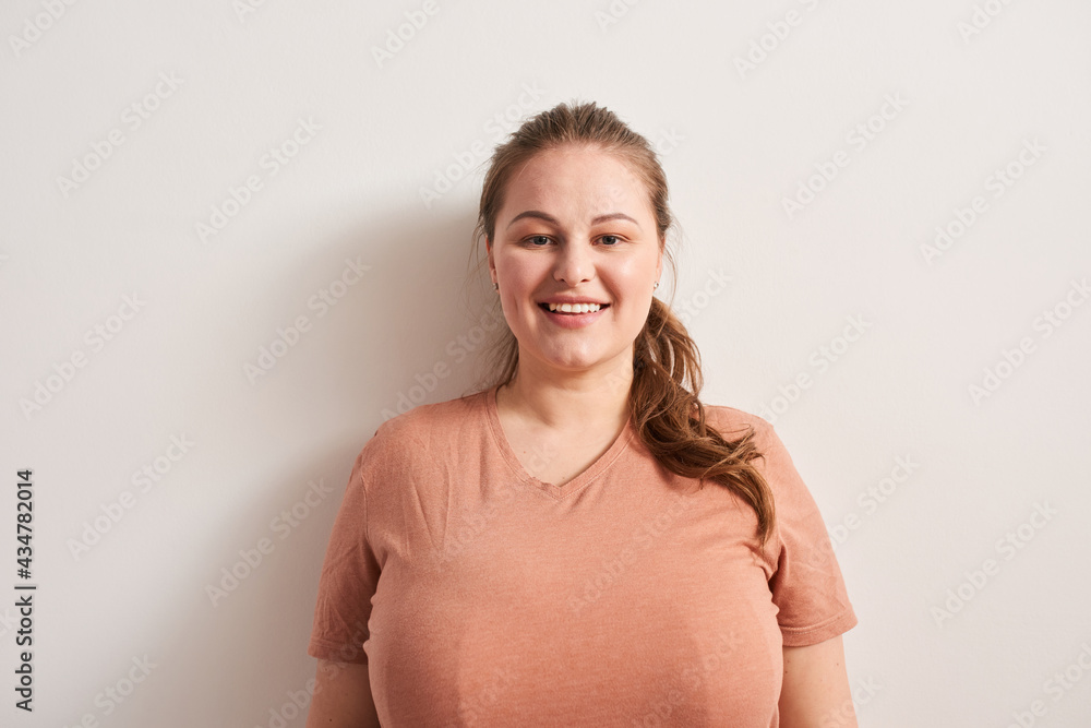 Fototapeta premium Woman in casual clothes is standing indoors and looking at camera with wide smile