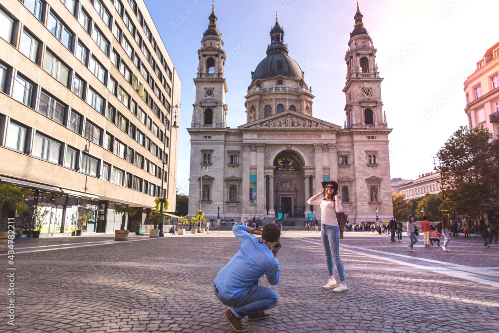 Young couple take pictures of each other while standing in front of St. Stephens Basilica in Budapest.