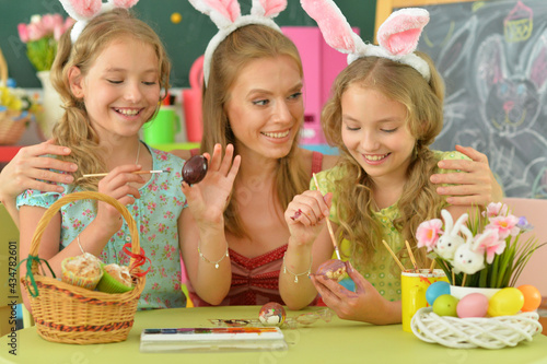  Mother with daughters wearing rabbit ears decorating Easter eggs