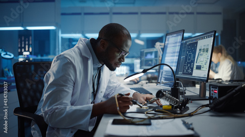 Modern Electronics Research, Development Facility: Black Male Engineer Does Computer Motherboard Soldering. Scientists Design PCB, Silicon Microchips, Semiconductors. Medium Closeup Shot