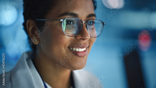 Portrait of Beautiful Black Latin Woman Computer Screen Reflecting in Her Glasses. Young Intelligent Female Scientist Working in Laboratory. Background Bokeh Blue with High-Tech Technological Lights