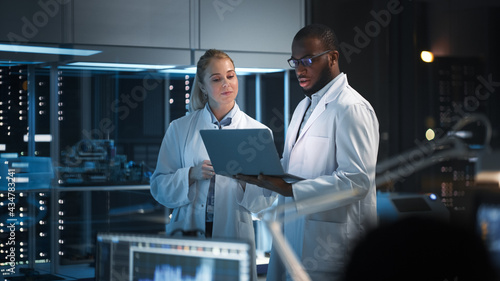 Modern Electronics Research, Development Facility: Engineer and Scientist Standing In High-Tech Laboratory, Use Laptop Computer, Talk, Design Silicon Microchips, Semiconductors, Manufacture Computers