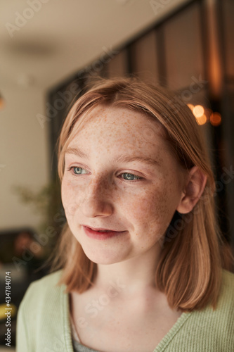 Freckled girl looking away while posing at her cozy flr during the sunny day photo