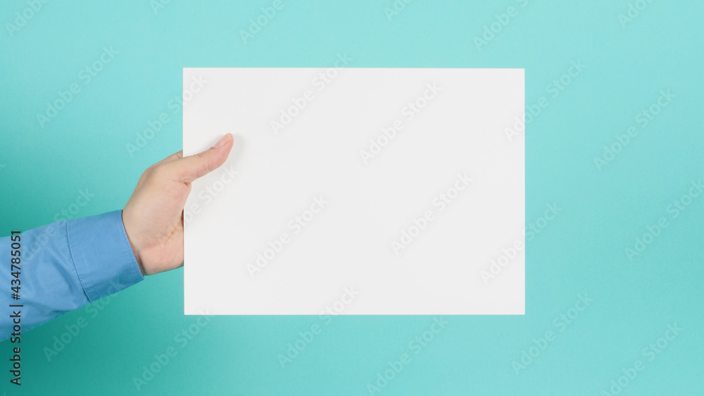 Hand is holding blank A4 paper and wear blue long sleeve shirt on green mint or Tiffany Blue background. Hand is holding blank A4 paper and wear blue long sleeve shirt on green mint or Tiffany Blue background.