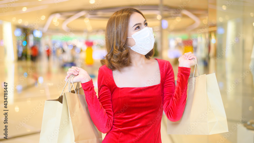 Young woman in red dress wearing protective mask in shopping mall, shopping under Covid-19 pandemic concept. Young woman in red dress wearing protective mask in shopping mall, shopping under Covid-19 pandemic concept.