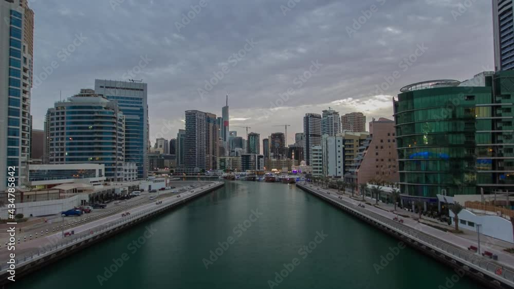 Dubai Marina waterfront with towers and yachts from bridge in Dubai night to day transition timelapse, United Arab Emirates. District with artificial canal and illuminated skyscrapers before sunrise Dubai Marina waterfront with towers and yachts from bridge in Dubai night to day transition timelapse, United Arab Emirates. District with artificial canal and illuminated skyscrapers before sunrise