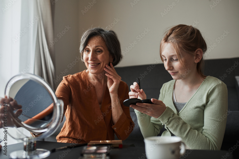 Woman looking at the mirror while her granddaughter preparing makeup for her Woman looking at the mirror while her granddaughter preparing makeup for her