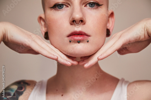 Woman with piercing at her face and ear tunnels posing with hands near her face