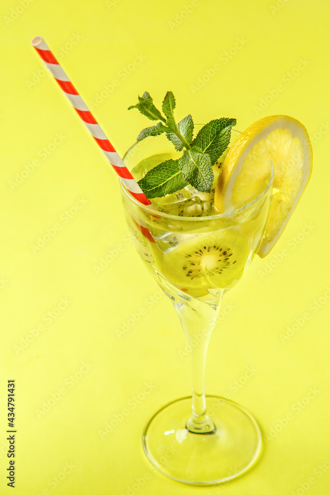 Kiwi cocktail decorated with lemon and mint in a glass on a napkin on a yellow background.