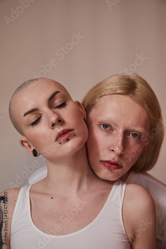 Womanlike albino man with long blonde hair holding head at the shoulder of bald masculine female