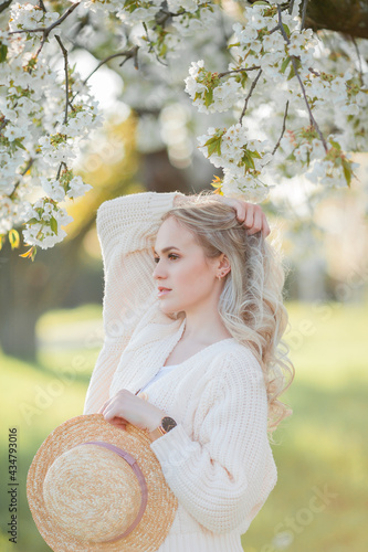 Beautiful young woman in a wicker hat is resting on a picnic in a blooming garden. White flowers. Spring. Happiness.