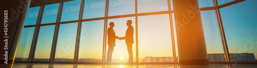 The two businessmen handshake in the office on the bright sun background