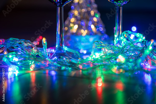 two glasses on the background of a shining Christmas tree and a multi-colored garland on a dark night background. New Year celebration.