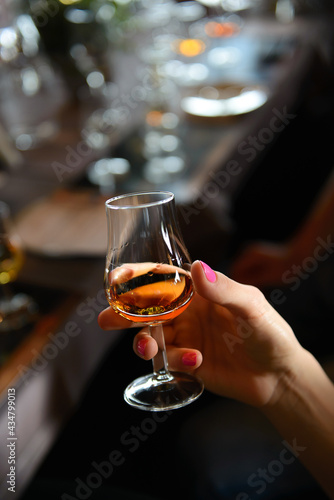 A glass with wiskey in hand of woman with blurred background. Concept of whiskey tasting. © Oskars