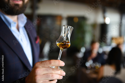 A glass with wiskey in hand of man with blurred background. Concept of whiskey tasting. © Oskars