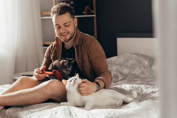 Man sitting at the bed with striped cat at the knees and stroking his white cat