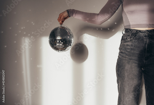 Unrecognizable woman holding disco ball in front of the white wall photo