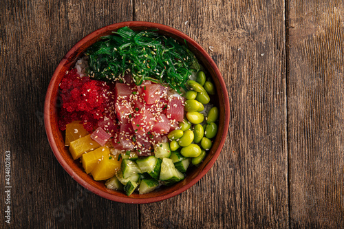 Hawaiian tuna poke bowl with vegetables on wooden background