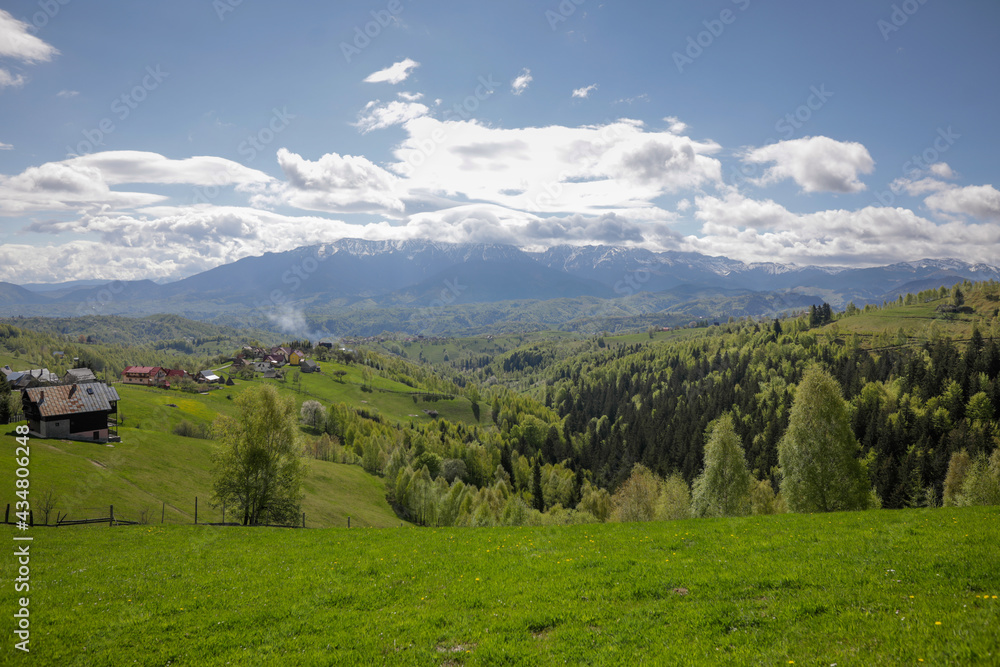 Rolling hills with villages and forests in Transylvania, Romania, with the Bucegi mountains in the background.