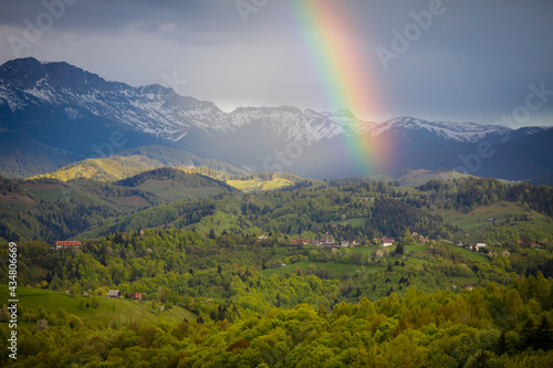 Rainbow over rolling hills with villages and forests in Transylvania, Romania, with the Bucegi mountains in the background.