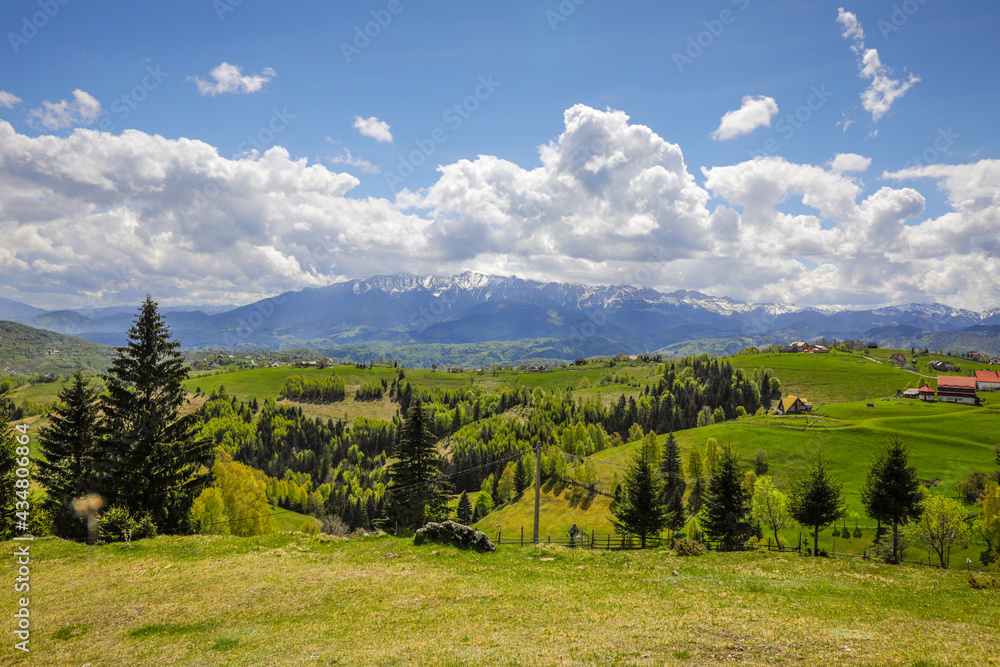 Rolling hills with villages and forests in Transylvania, Romania, with the Bucegi mountains in the background.