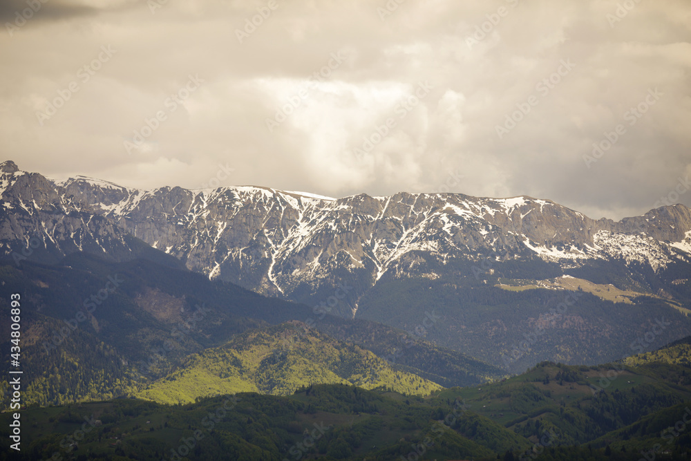 Naklejka premium Heavy clouds over the Bucegi mountains in Romania during a spring day, as seen from the hills of Pestera village in Transylvania.