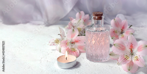 Mock up spa aromatherapy concept with perfume glass or aroma oil glass, flowers and candle on light background. Massage. Wellness. Spring greeting card for Mothers day or wedding.