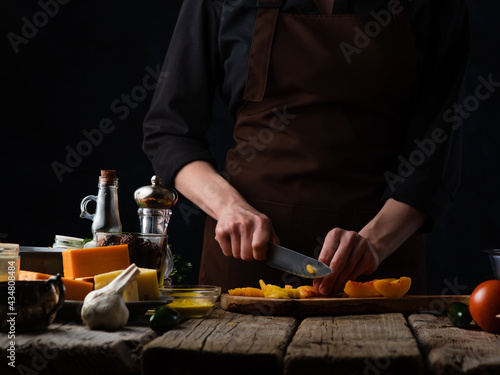 Stuffed goose. The chef is cutting oranges on a cutting board. There are also ingredients in the frame: garlic, cheese, sauce, spices. A festive dish. Bright paints, dark background.