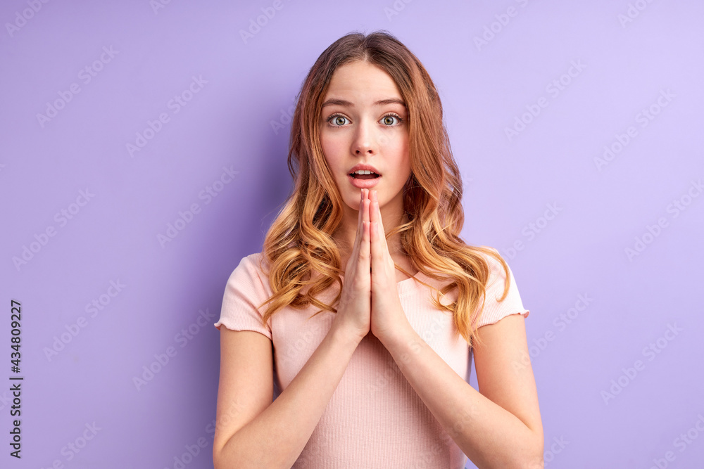 Attractive blonde girl in casual clothes prays for wellness of family, keeps palms pressed together in praying gesture, dreaming. Studio shot, purple background. Mock up copy space Attractive blonde girl in casual clothes prays for wellness of family, keeps palms pressed together in praying gesture, dreaming. Studio shot, purple background. Mock up copy space