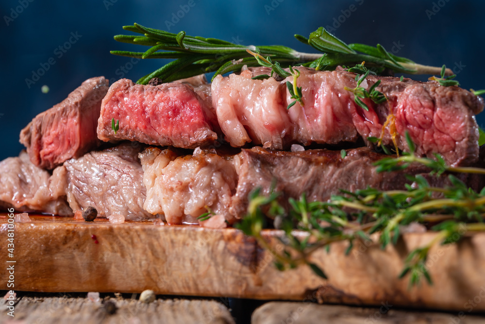 The photo shows a fragrant, juicy steak on a piece of bread. The steak is decorated with sprigs of greenery. Wooden table. Dark blue background. Close-up..