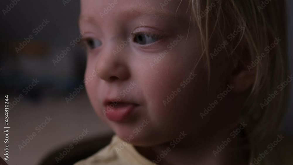 Little girl eats a bun and says something. Large portrait of a blond child. Baby eats enthusiasticall. Portrait in a low key