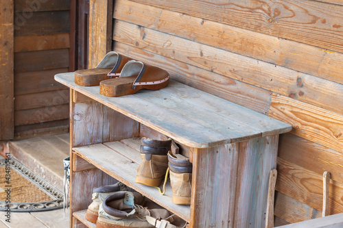 Old wooden shoebox near a wooden cottage on a farm. The shoe box has old clogs, rubber boots and shoes. photo