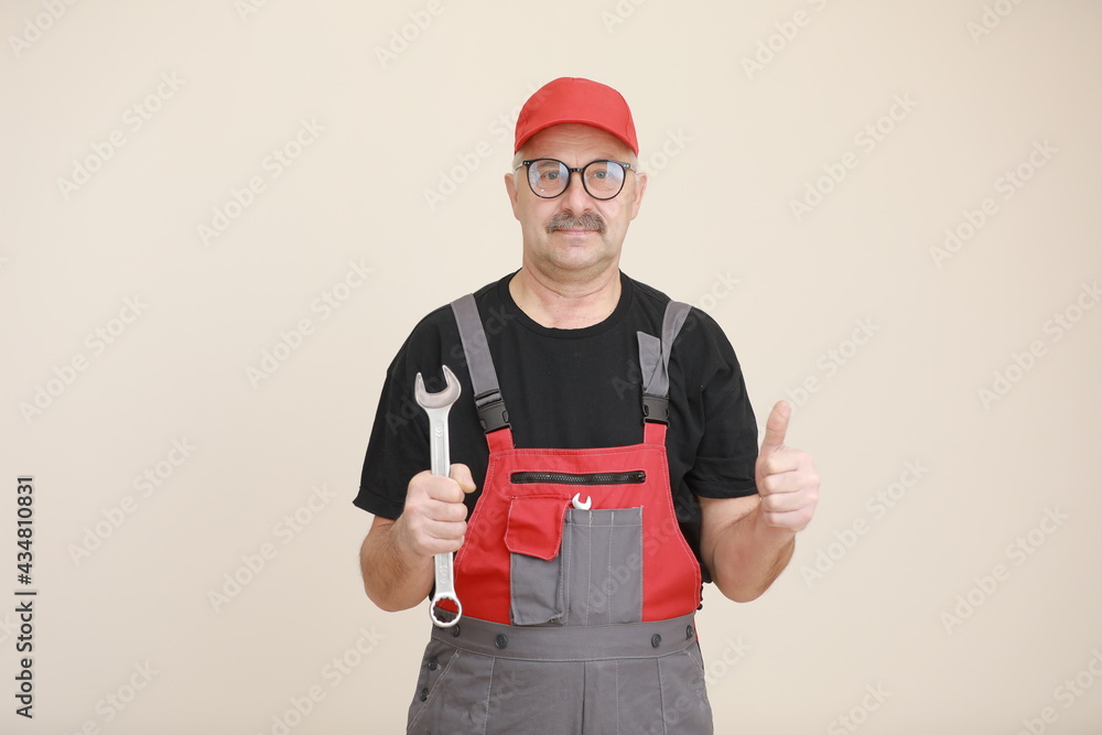 man worker in a black t shirt, glasses and red gray construction overall holds a new gray tool straight pipe wrench or spanner and giving a thumbs up on a white isolated background