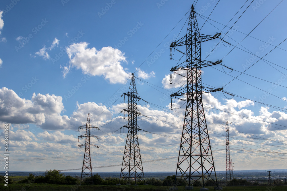 High voltage electric towers in a row with cloudy blue sky background