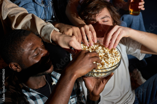 Fun Movie with Friends. Group of people eating popcorn while watching movie on tv  at home  taking popcorn from bowl  enjoy weekends. close-up popcorn