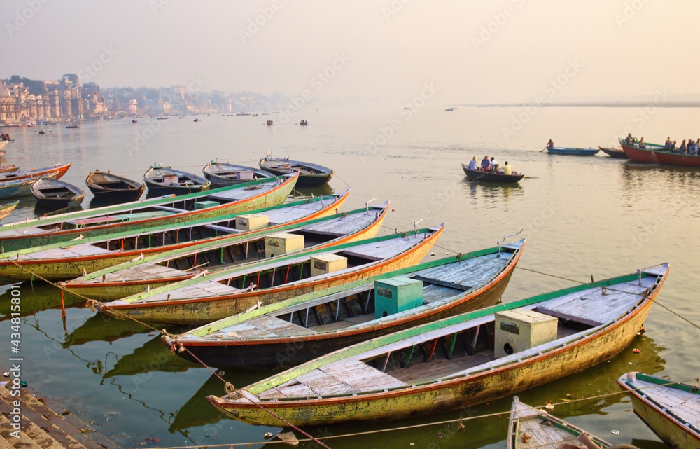 Varanasi, India : Bunch of old wooden colorful boats docked in the bay of Ganges river bank during sunset sunrise against foggy weather. The holy place for hindu religion.