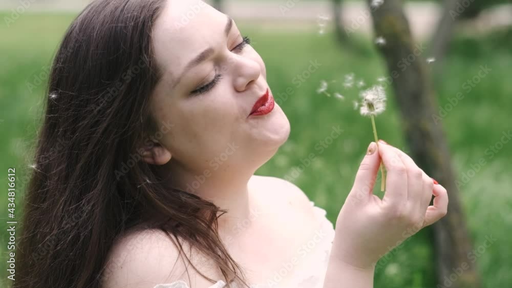 Portrait of a beautiful young woman blowing on the ripened dandelion in the park Portrait of a beautiful young woman blowing on the ripened dandelion in the park