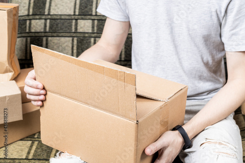 male person indoors unpack cardboard parcel package. men opening box. delivery service concept. online shopping conceptual © Andrii