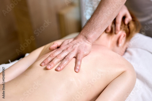 Redhead lady lying on stomach at spa  getting massage on neck and back by professional male masseur. indoors  at spa center