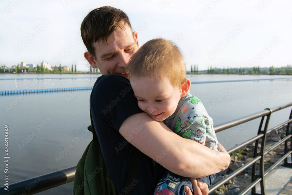 Fototapeta premium Smiling and happy father hugs the child. Cheerful family by the river