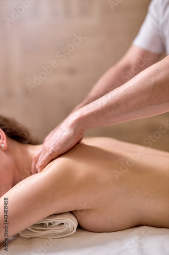 Young female at spa resort, receiving massage on neck and shoulders muscles, enjoying time in spa center, cropped professional masseur at work. Focus on hands and back