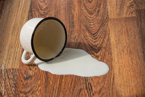 metal mug with milk dropped on the floor spilled milk stain on the wooden floor photo