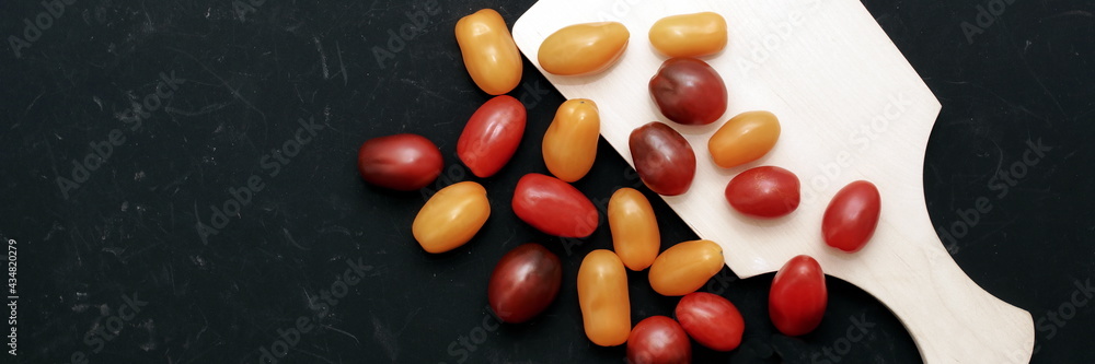 Plum Cherry Tomatoes On White Cutting Board. Assorted Plum Cherry Tomatoes On Wooden Cutting Board. Scattered Red, Yellow And Black Plum Cherry Tomato On Black Shabby Background. Plum Cherry Tomatoes On White Cutting Board. Assorted Plum Cherry Tomatoes On Wooden Cutting Board. Scattered Red, Yellow And Black Plum Cherry Tomato On Black Shabby Background.