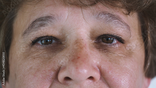 Close up of 50 years female face with Beautiful brown Eyes, Large wrinkles on the old woman's face. Natural Beauty with Freckles. Gorgeous woman with long Eyelashes and Attractive Appearance