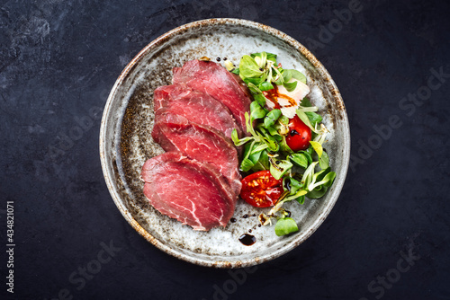 Modern style gourmet raw Japanese tataki beef filet with lettuce and tomatoes as top view on a Nordic design plate with copy space