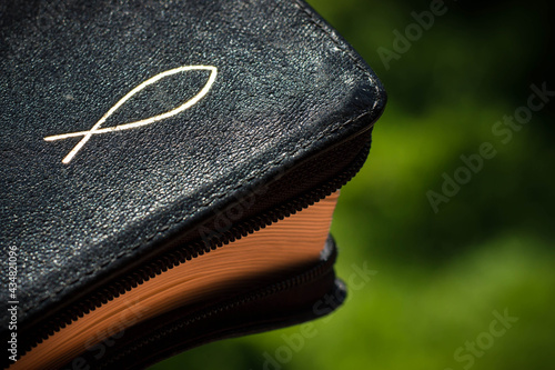 Bible with a christian fish symbol on the black cover with green background photo