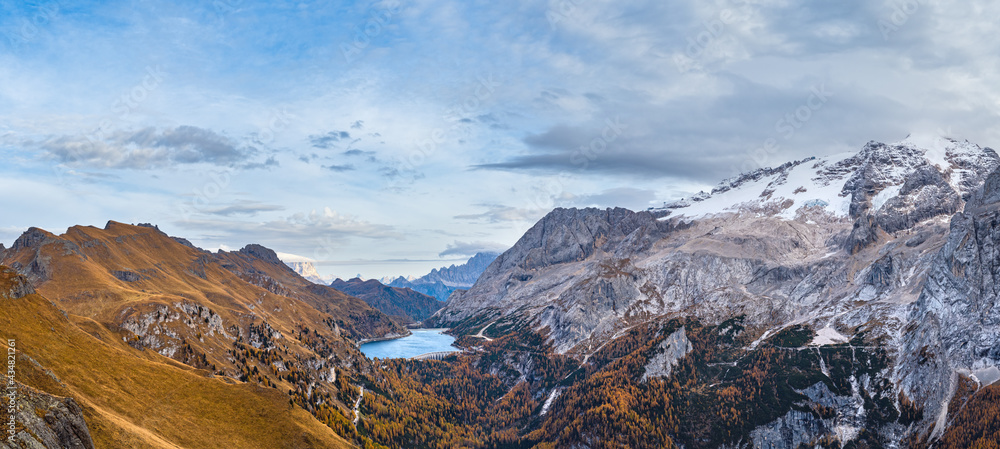 Autumn Dolomites mountain scene from hiking path betwen Pordoi Pass and Fedaia Lake, Italy. Snowy Marmolada Glacier and Fedaia Lake in far.
