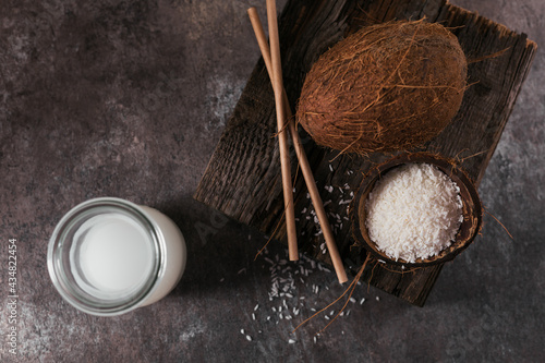 Bottle of coconut vegan milk with straws, whole coconut and flakes on dark background. Healthy lifestyle concept.