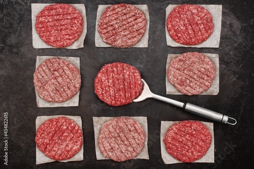 Uncooked Ground Beef Patties for Grilling. Raw Minced Steak Burgers from Beef and Pork Meat on Black Background. BBQ Grill Tools with Raw Beef Hamburger Patties. Raw Burger Cutlets.