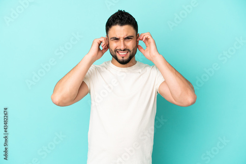 Young arab man isolated on blue background frustrated and covering ears